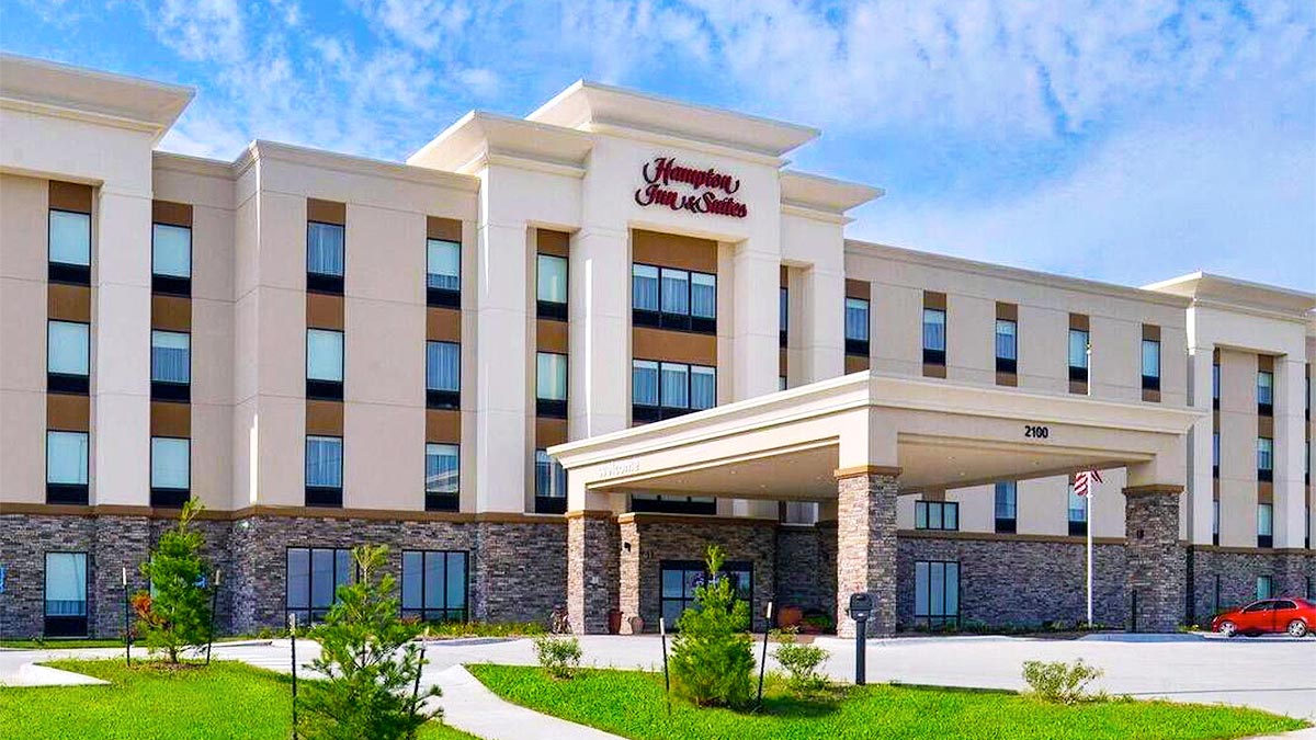 exterior of Hampton Inn and Suites Valdosta Conference Center with red car parked at side during day with blue sky and clouds in Valdosta, Georgia, USA